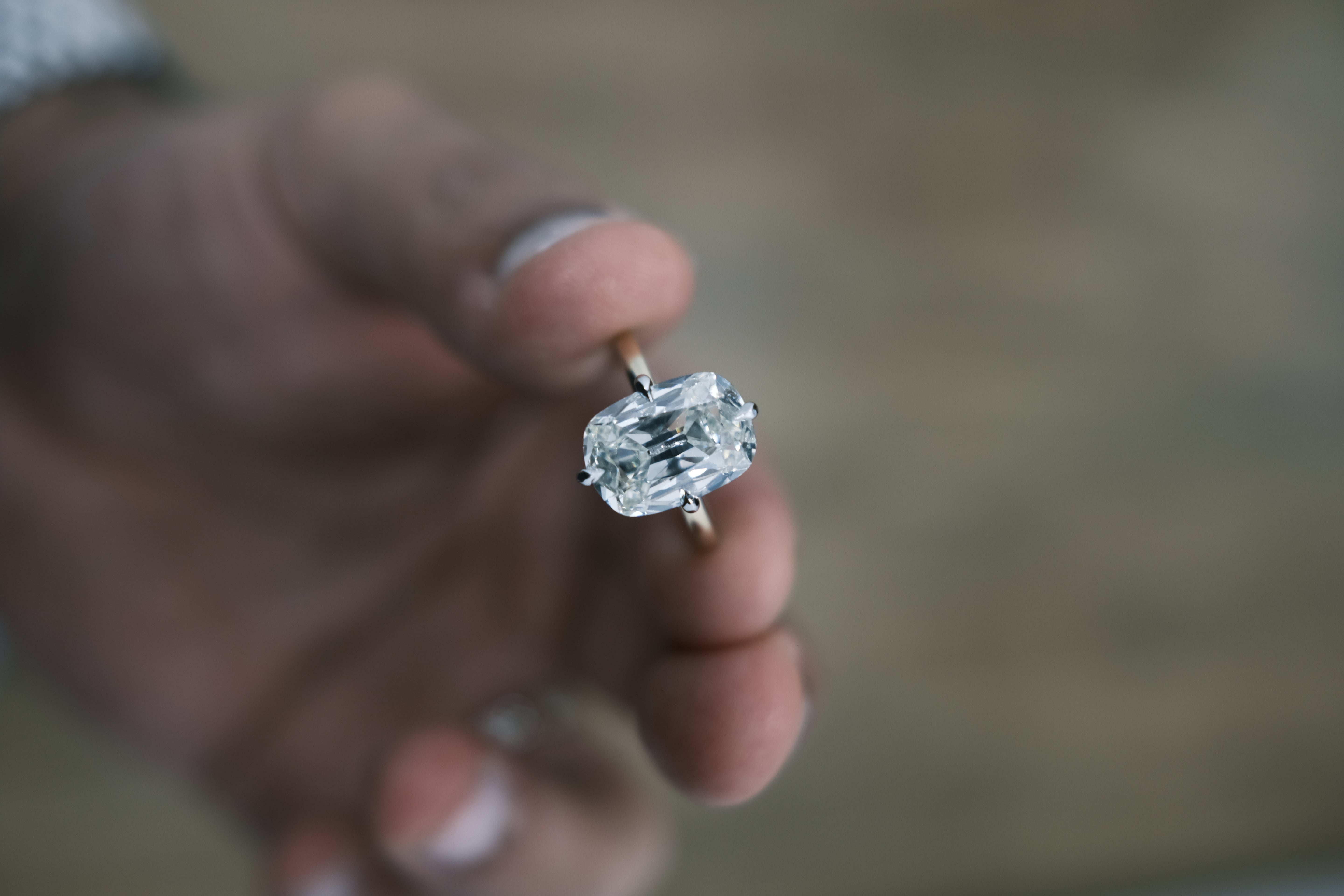 Diamond ring held between fingers with a blurred background